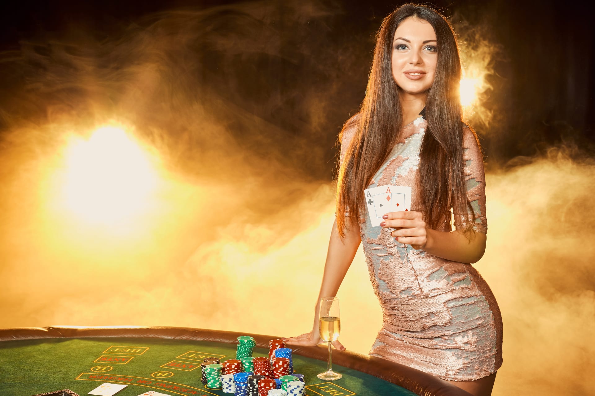 gorgeous young woman evening dress with two cards hands standing near poker table with glass of champagne